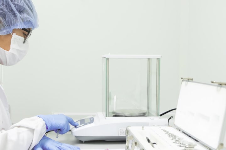 Über uns 3 Der Bediener drückt die Tastatur der Analysenwaage, um die Waagschale für den Kalibrierungstest zu tarieren.